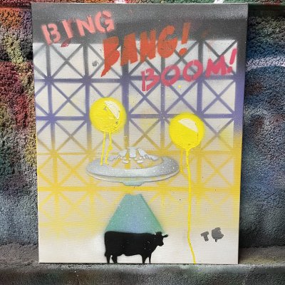 A spray-painted canvas reading Bing Bang Boom, with yellow balloons, a flying saucer beaming up a cow and a scaffolding pattern, leaning on a graffiti wall.