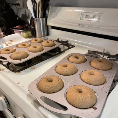 Two trays of freshly baked donuts on a white stovetop.