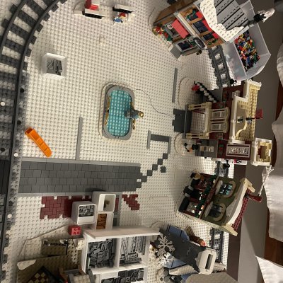 Top-down view of the LEGO winter village, with the train track looping around white baseplates, buildings and a blue ice rink.