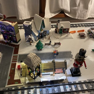 A LEGO winter village street with snowy houses, a Christmas tree, a train station and a giant nutcracker beside the tracks.