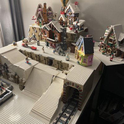 A raised LEGO village section with snowy chalets and a hot air balloon above a train tunnel carved into the hillside.