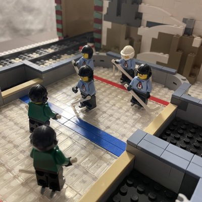 LEGO minifigures playing hockey on a rink built from transparent and white bricks.