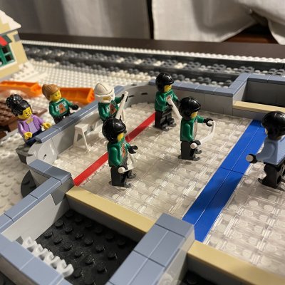 Close-up of LEGO hockey players in green and blue jerseys on the rink, with the train track behind them.