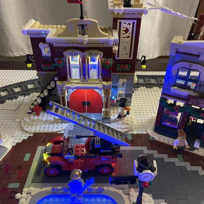 Overhead view of the LEGO fire station with red doors, the fire truck with its ladder raised and the skating pond.