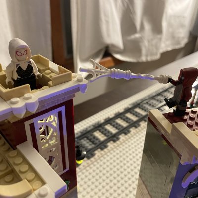 LEGO Spider-Gwen perched on a rooftop while another minifigure swings in on a web line.