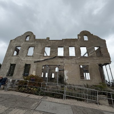 The roofless, burned-out shell of the warden's house under a cloudy sky.