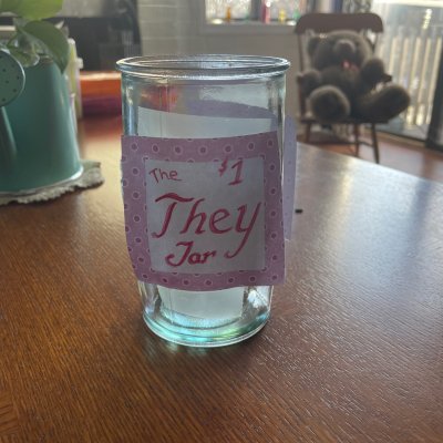 A glass jar on a wooden table, labeled The They Jar $1.