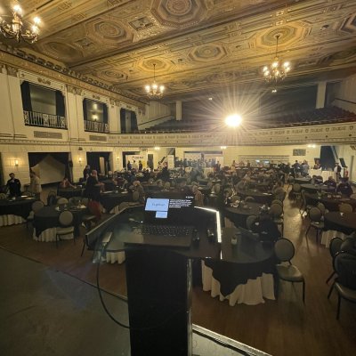 A conference ballroom with an ornate gold ceiling and chandeliers, seen from behind the podium.